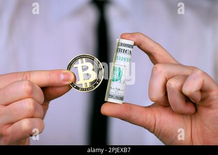 Ein Geschäftsmann, der Bitcoin und ein Bündel Dollar in der Hand hält. Stockfoto