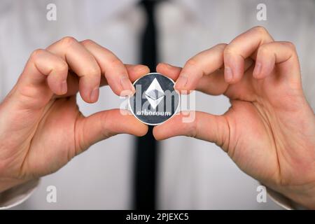 Ein Geschäftsmann mit weißem Hemd und schwarzer Krawatte hält eine physische Version von ethereum in seinen Händen. Stockfoto