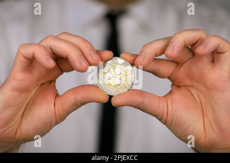 Ein Geschäftsmann in einem weißen Hemd und einer schwarzen Krawatte hält eine physische Version der Kryptowährung xrp in seinen Händen. Stockfoto