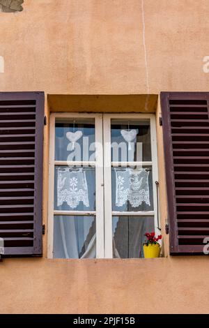 Fenster mit dekorativen Bezügen aus Nadelarbeit, herzförmig. Blick auf die Straße, Cortona, Italien Stockfoto
