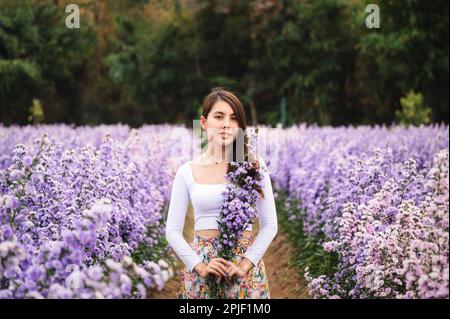 Wunderschöne junge asiatische Frau, die margaretenblume im blühenden Garten hält Stockfoto