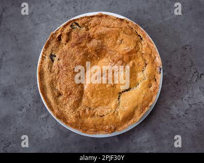 Ein hausgemachter klassischer Apfelkuchen, auch als holländischer Apfelkuchen bekannt, mit knuspriger Kruste und auf einem dunklen Tischhintergrund zentriert. Ansicht von oben nach unten Stockfoto