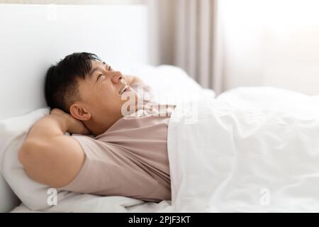 Positiv glücklicher asiatischer Mann, der zu Hause im Bett lag und träumte Stockfoto