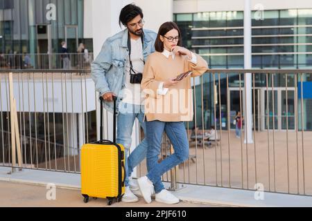 Verzweifeltes, pensives, junges, multiethnisches Paar in lässiger Kleidung und Brille mit Pass, Tickets und Koffer denken am Flughafen Stockfoto