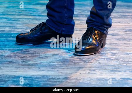 Herrenbeine in Bühnenhose mit Streifen und Lederschuhen für irische Tänze auf dem Boden. Schwarze Arbeitsschuhe für Stepptanz mit Reflexion Stockfoto