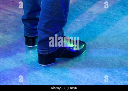 Herrenbeine in Bühnenhose mit Streifen und Lederschuhen für irische Tänze auf dem Boden. Schwarze Arbeitsschuhe für Stepptanz mit Reflexion Stockfoto