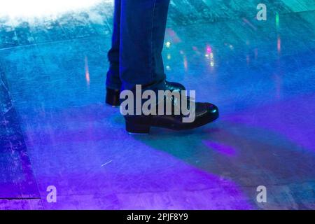 Herrenbeine in Bühnenhose mit Streifen und Lederschuhen für irische Tänze auf dem Boden. Schwarze Arbeitsschuhe für Stepptanz mit Reflexion Stockfoto