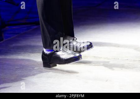 Herrenbeine in Bühnenhose mit Streifen und Lederschuhen für irische Tänze auf dem Boden. Schwarze Arbeitsschuhe für Stepptanz mit Reflexion Stockfoto