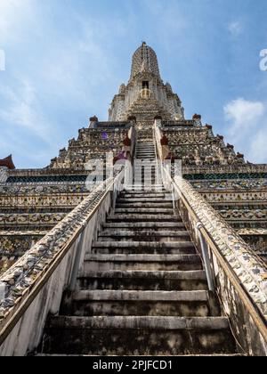 Steile Treppen, die zum Wat Arun Tempel, dem Tempel der Morgenröte, in Bangkok, Thailand führen, mit seinem Turm, der in Richtung eines blauen Himmels zeigt. Stockfoto