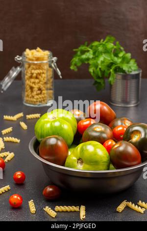 Verschiedene Sorten grüner und roter Tomaten in einer Metalldose. Pasta in einem Glas und Petersilie in einem Glas. Stockfoto