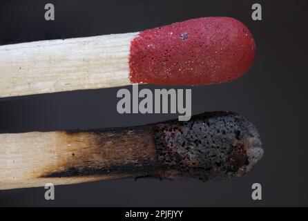 Makro extreme Nahaufnahme von zwei Holzstücken passt zu einem roten Streichkopf und daneben ein verbranntes verkohltes Bild vor dunkelgrauem Hintergrund als Konzept für Fi Stockfoto