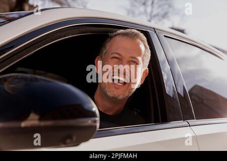 Glücklicher, lächelnder, attraktiver Geschäftsmann in einem lässigen Stoff, der ein Auto in der Stadt fährt, Probefahrt Stockfoto