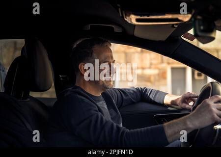 Glücklicher, lächelnder, attraktiver Geschäftsmann in einem lässigen Stoff, der ein Auto in der Stadt fährt, Probefahrt Stockfoto