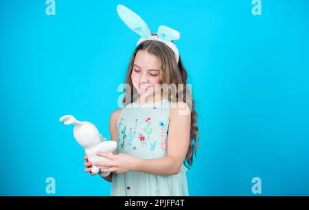 Bleib ruhig und fröhliche Ostern. Kleines Mädchen und Kaninchenspielzeug. Kleines Mädchen in Kaninchenohren mit Osterspielzeug. Kleines Kind im Osterhasen-Stil, mit dem gespielt wird Stockfoto