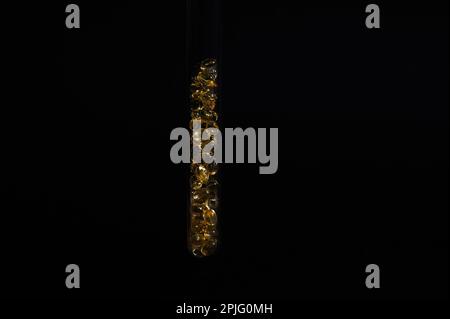 Stillleben. Reagenzglas im Labor gefüllt mit Weichgelkapseln mit Omega 3 Öl, Vitamin D auf isoliertem schwarzem Hintergrund Stockfoto