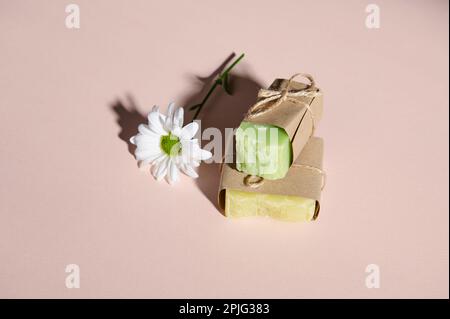 Handgefertigte, umweltfreundliche Seifenriegel mit natürlichen Inhaltsstoffen und Kamillenblüten, isolierter pinkfarbener Pastellhintergrund Stockfoto