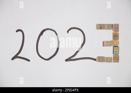 2023 ist mit einem schwarzen Marker beschriftet, und die Nummer drei ist aus Micro-sim-Karten auf weißem Hintergrund aufgebaut, einem mobilen Unterstützer im neuen Jahr 20 Stockfoto
