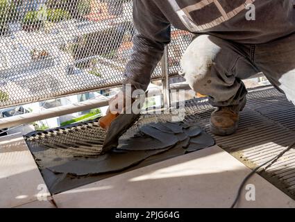 Maurer bereitet Zement auf einer Platte mit einer gekerbten Kelle vor. Ich arbeite in einer Baustelle. Arbeitskonzept, Handel. Stockfoto