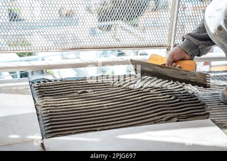 Maurer bereitet Zement auf einer Platte mit einer gekerbten Kelle vor. Ich arbeite in einer Baustelle. Arbeitskonzept, Handel. Stockfoto