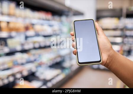 Nahaufnahme einer weiblichen Hand, die ein Smartphone mit leerem Bildschirmmodell im Innenraum eines Supermarkts zeigt Stockfoto