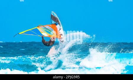 Sommersport: Ein Windsurfer, der einen akrobatischen Sprung in die Wellen macht und das Meerwasser besprüht Stockfoto
