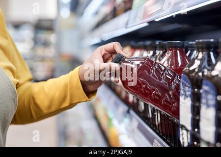 Nahaufnahme einer Arbeiterin, die Flaschen in Regalen im Supermarkt für Getränke und Säfte bereitstellte Stockfoto