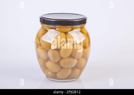 Glas mit Mandelfüllung aus grünen Oliven auf weißem Hintergrund. Glas mit Knoblauch-gefüllten Oliven, isoliert auf weiß. Stockfoto