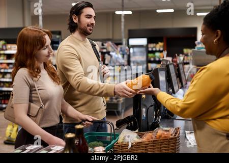 Seitliches Porträt eines jungen Paares, das an der Kasse im Supermarkt steht und Lebensmittel einkauft Stockfoto