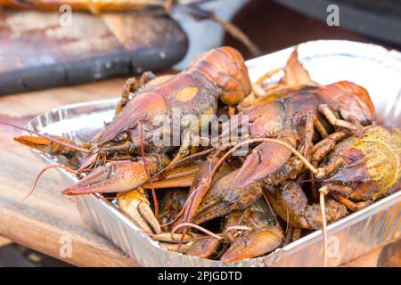 Gekochte Flusskrebse werden auf eine Einweg-Folienplatte auf der Theke gelegt. Street Food, Fast Food. Stockfoto