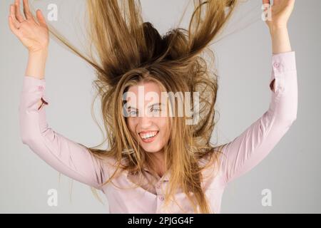 Lächelnde Frau mit langen, zerklüfteten Haaren. Haarpflege. Glückliches Mädchen mit winkenden Haaren. Modefrau Frisur. Weibliches Model mit ungebürstetem, trockenem Haar Stockfoto
