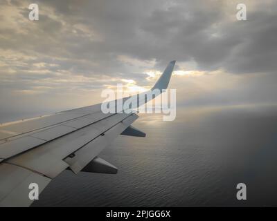 Wolken und Sonnenuntergang vom Flugzeugfenster auf dem Flügel während eines Fluges zu sehen Stockfoto