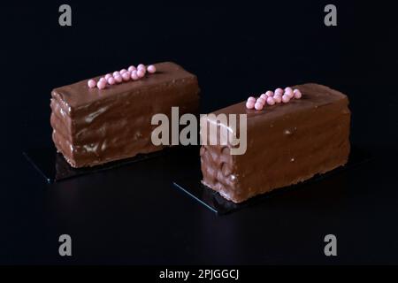 Zwei Mousse-Schokoladen-Desserts mit Schokoladencreme und Himbeermarmelade überzogene Gourmet-Schokoladenglasur auf schwarzem Hintergrund Stockfoto