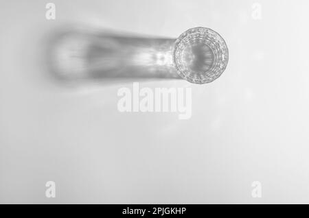 Ein Glas mit Wasser und scharfen Schatten, kaustischer Effekt, wenn Licht auf hellem Hintergrund durchdringt Stockfoto