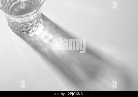 Ein Glas mit Wasser und scharfen Schatten, kaustischer Effekt, wenn Licht auf hellem Hintergrund durchdringt Stockfoto