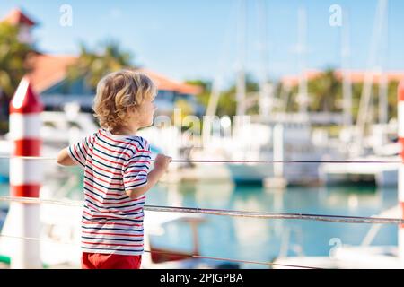 Kinderbeobachtungsyacht und Boot im Hafen. Yachtsport für Familien mit Kindern. Kleiner Junge, der in den Sommerferien in einem tropischen Resort herumläuft. Stockfoto