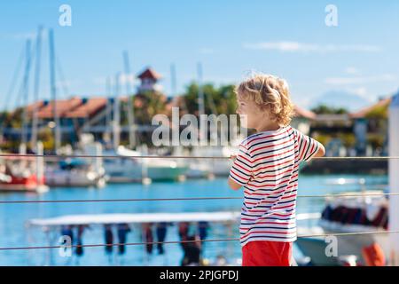 Kinderbeobachtungsyacht und Boot im Hafen. Yachtsport für Familien mit Kindern. Kleiner Junge, der in den Sommerferien in einem tropischen Resort herumläuft. Stockfoto