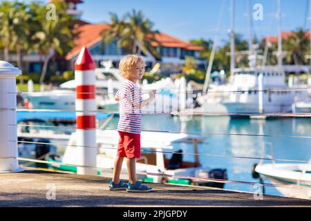 Kinderbeobachtungsyacht und Boot im Hafen. Yachtsport für Familien mit Kindern. Kleiner Junge, der in den Sommerferien in einem tropischen Resort herumläuft. Stockfoto