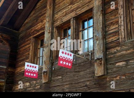 Zwei Flaggen des Kantons Wallis im Fenster eines Schweizer Chalets, Blatten bei Naters, Wallis, Schweiz Stockfoto