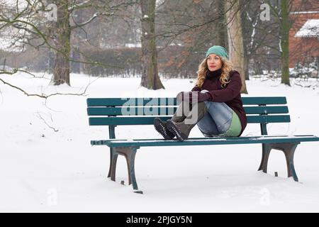 Einsame Frau, die im Winter auf einer schneebedeckten Parkbank sitzt Stockfoto
