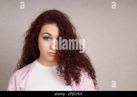 Traurige Teenager suchen gedrückt versteckt sich die Hälfte der ihr Gesicht hinter den langen, lockigen Haar Stockfoto