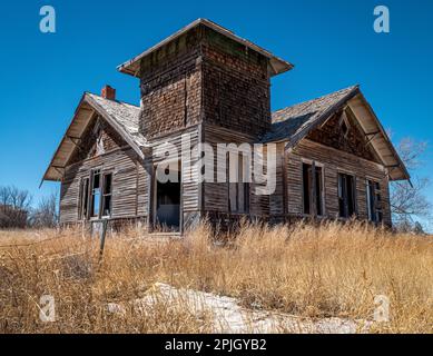 Dieses verlassene und vernachlässigte Haus, oder vielleicht eine alte Schule, liegt verlassen in einem ländlichen Dorf im Nordosten von New Mexico. Stockfoto