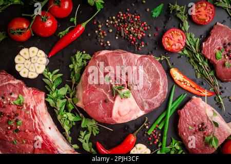 Verschiedene Steaks. Gemischtes rohes Fleisch auf schwarzem Kreidetafelhintergrund. Rib-Eye-Steak auf dem Knochen, Kalbsschenkel (Ossobuco), Filet mit Stockfoto