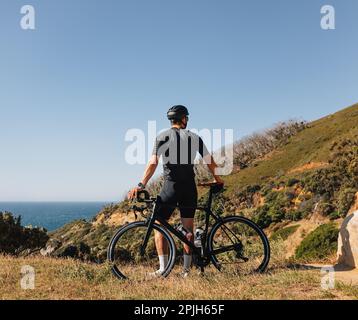 Rückansicht eines männlichen Radfahrers, der sich während des Trainings auf seinem Road Bike lehnt und die Aussicht genießt Stockfoto