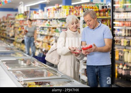 Reifes Paar, das im Supermarkt einkauft und gefrorene Fertiggerichte für ein schnelles Abendessen auswählt Stockfoto