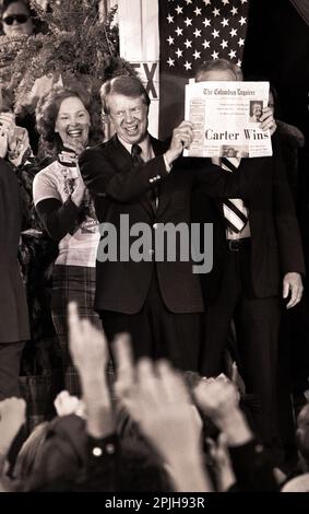 Carter Cousin Betty Pope reagiert, als der designierte Präsident Jimmy Carter eine Zeitung mit der Überschrift „Carter gewinnt“ hält, während er in der Wahlnacht mit Menschenmassen in den Straßen von Tiny Plains, Georgia, feiert. Stockfoto