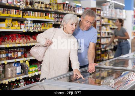 Reifes Paar, das im Supermarkt einkauft und gefrorene Fertiggerichte für ein schnelles Abendessen auswählt Stockfoto