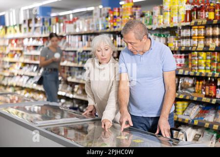 Reifes Paar, das im Supermarkt einkauft und gefrorene Fertiggerichte für ein schnelles Abendessen auswählt Stockfoto