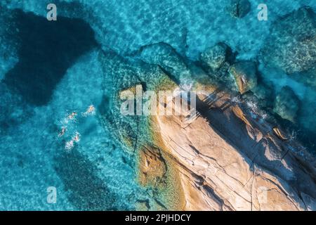 Luftaufnahme von schwimmenden Personen im blauen Meer, felsigem Strand, Wellen Stockfoto
