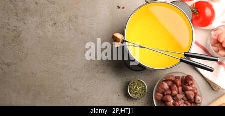 Flache Laienzusammensetzung mit Fondue-Topf und Fleisch auf grauem Tisch, Platz für Text. Bannerdesign Stockfoto