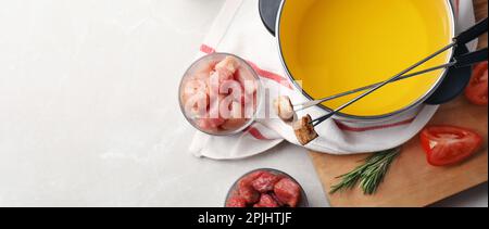 Flache Laienzusammensetzung mit Fondue-Topf und Fleisch auf einem leichten Tisch, Platz für Text. Bannerdesign Stockfoto